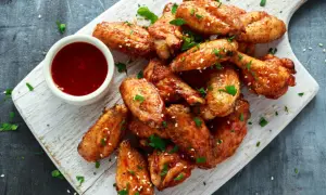 Deliciosas alitas de pollo fritas, doradas y crujientes, servidas con salsa y perejil picado.