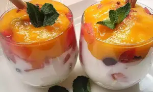 Dos copas de cristal con capas de yogur blanco, trozos de fruta roja y un delicioso mousse de mango coronado con menta y canela.