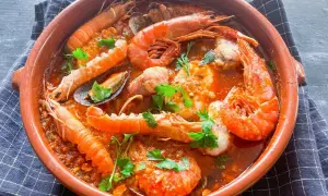 Zarzuela de pescado en cazuela de barro, con gambas, cigalas, mejillones y trozos de pescado en salsa roja, decorada con perejil.