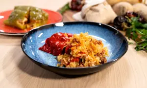 Plato azul con pimientos rellenos de arroz y carne. Otro pimiento verde relleno en un plato rojo al fondo.