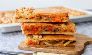Tres porciones de empanada de verduras apiladas, con relleno de pimientos, calabacín y tomate.