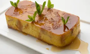 Pan de Calatrava, un postre dorado con caramelo líquido y hojas de menta, servido en una bandeja blanca.