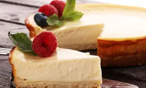 Deliciosa tarta de queso con galletas, coronada con frambuesas frescas y hojas de menta. Un trozo ya servido en un tenedor.