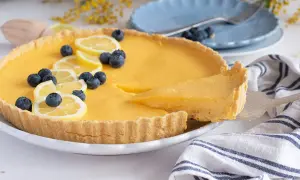 Deliciosa tarta de limón, decorada con rodajas de limón y arándanos. Una porción se sirve con una espátula.