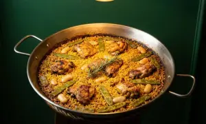 Paella valenciana recién hecha, con trozos de pollo dorado, judías verdes y garrofón, coronada con una ramita de romero.