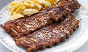 Costillas de cerdo jugosas y doradas, cubiertas de salsa brillante, acompañadas de papas fritas crujientes en un plato blanco.