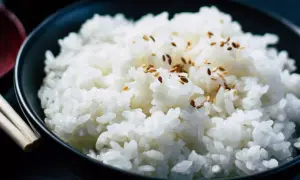 Un tazón de arroz blanco humeante, espolvoreado con semillas de sésamo, listo para ser disfrutado con palillos.