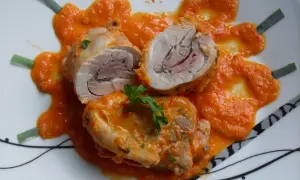Contramuslos de pollo Thermomix enrollados con jamón, cubiertos de salsa de pimientos y decorados con perejil y cebolleta.