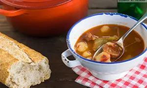 Un reconfortante plato de patatas a la riojana, con chorizo y pimientos, servido en un cuenco blanco con borde azul.