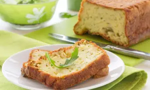 Rebanadas de un delicioso pastel de calabacín, esponjoso y dorado, servidas en un plato blanco con una hoja verde.