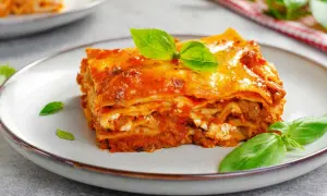 Porción de lasaña de carne con capas de pasta, salsa de tomate y queso, decorada con hojas de albahaca fresca.