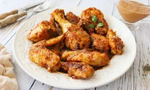 Plato de pollo a la coca cola, jugoso y caramelizado, con un toque de perejil. Servido en una fuente blanca sobre una mesa de madera.