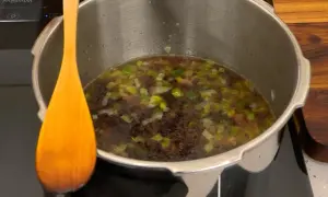 Olla express con alubias y verduras, lista para el tiempo de cocción. Una cuchara de madera descansa a un lado.
