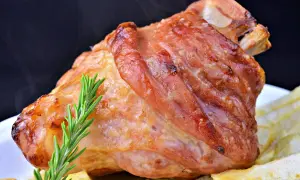 Codillo de cerdo asado, dorado y jugoso, servido con patatas fritas y una ramita de romero.