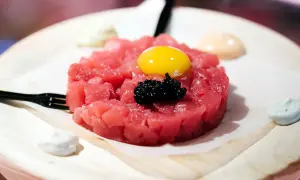 Delicioso tartar de atún fresco, coronado con yema de huevo y caviar negro. Servido con salsas cremosas y un tenedor.