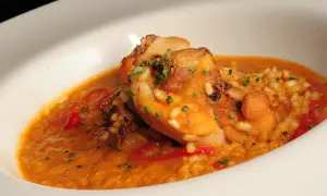 Delicioso arroz con conejo, trozos dorados de carne y pimientos rojos en una cremosa salsa, adornado con cebollino fresco.