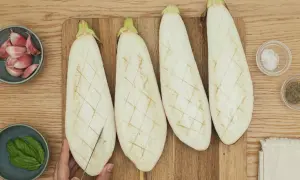 Cuatro mitades de berenjena cortadas en rejilla, listas para ser rellenas. A su lado, ajo, albahaca, sal y pimienta.
