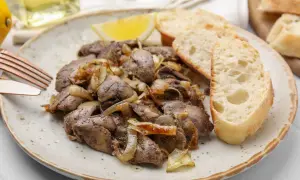 Deliciosos higaditos de pollo encebollados servidos con pan crujiente y una rodaja de limón.