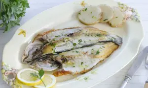 Lubina a la plancha, dorada y jugosa, servida con patatas y rodajas de limón. Un plato sencillo y delicioso.