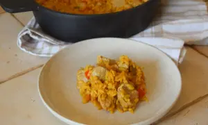Un plato de arroz con carne, pimientos y trozos de cerdo, servido desde una paellera.