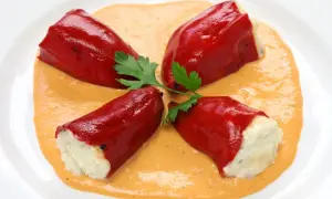 Cuatro pimientos rojos rellenos de bacalao, servidos sobre una cremosa salsa naranja y decorados con perejil.