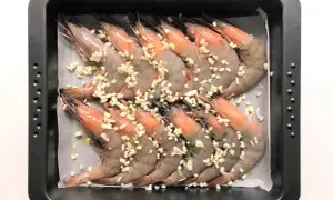 Langostinos al horno listos para cocinar, cubiertos con ajo picado en una bandeja.