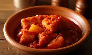 Bacalao a la vizcaina, trozos de pescado blanco en una salsa roja con pimientos y cebolla, servido en un cuenco de barro.