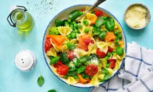 Un plato de pasta con verduras frescas: brócoli, guisantes, tomates cherry y zanahoria, espolvoreado con queso rallado.