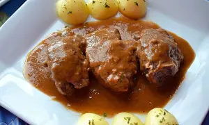 Carrilleras de ternera estofadas en salsa, acompañadas de patatas cocidas y espolvoreadas con perejil. Un plato casero y reconfortante.