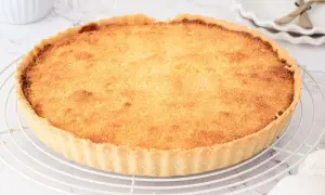 Tarta de coco dorada y crujiente sobre una rejilla. Su relleno esponjoso y aroma tropical invitan a probar esta delicia.