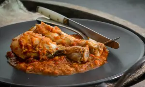 Dos muslos de pollo al chilindrón, servidos en un plato oscuro con cubiertos.