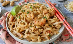 Un delicioso plato de pad thai con camarones, fideos de arroz, cacahuetes picados y cebollino.