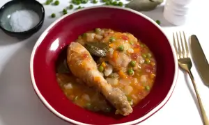 Un delicioso pollo a la jardinera en un cuenco rojo, con guisantes, zanahoria y laurel.