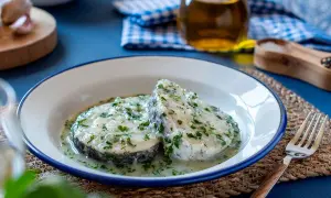 Dos rodajas de merluza en salsa verde, con perejil picado y una cremosa salsa. Un plato casero listo para disfrutar.