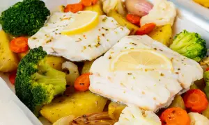 Bacalao al horno con patatas, brócoli, zanahorias y coliflor, todo asado en una bandeja.