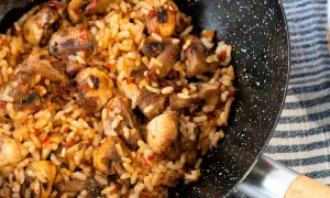 Arroz con champiñones recién hecho en sartén, con trozos dorados de champiñones y un toque de pimiento rojo.