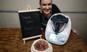 Mujer sonriente junto a una tarta San Marcos y una Thermomix. La pizarra anuncia "Tarta San Marcos".