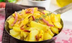 Patatas al microondas con trocitos de bacon crujiente y romero fresco, servidas en una sartén metálica. ¡Un plato sencillo y delicioso!
