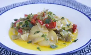 Patatas a lo pobre con pimientos rojos y verdes, cebolla y perejil, servidas en un plato blanco con borde azul.