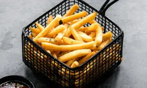 Cesta negra llena de crujientes patatas fritas doradas, listas para ser disfrutadas con una salsa roja.