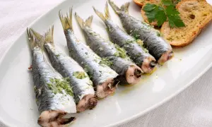 Cinco sardinas al horno, preparadas con hierbas y ajo, servidas en una bandeja blanca con tostadas.