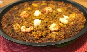 Arroz de tamboril con gambas y trozos blancos de pescado, servido en una paellera negra sobre una alfombrilla roja.