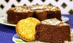 Un trozo de bizcocho de chocolate espolvoreado con azúcar glas junto a una galleta tipo Príncipe.
