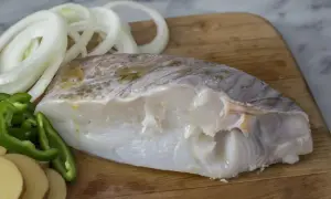 Filete de bacalao fresco con rodajas de patata, pimiento verde y cebolla, listo para preparar deliciosas recetas de bacalao.