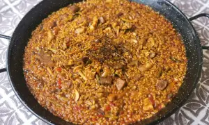 Arroz con secreto, un plato de paella con trozos de carne, pimientos y judías verdes, coronado con hierbas aromáticas.