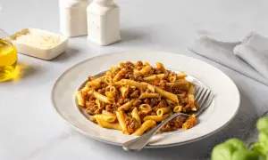Un plato de macarrones a la boloñesa, con un tenedor listo para disfrutar. Acompañan aceite de oliva, queso rallado y saleros.