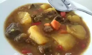 Un plato humeante de patatas con carne olla express, con trozos de zanahoria y pimiento rojo.