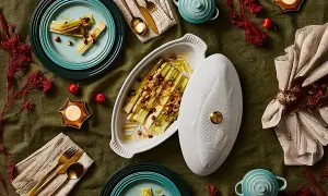 Puerros al horno, tiernos y dorados, servidos en una elegante fuente con tapa en forma de pez. Decoración festiva con velas y frutos rojos.