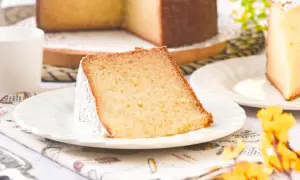 Rebanada de bizcocho de leche caliente, esponjoso y espolvoreado con azúcar glas, servido en plato blanco.