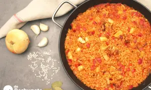 Paella de arroz con calamares, pimientos rojos y especias. Ingredientes frescos como cebolla y ajos acompañan este delicioso plato.